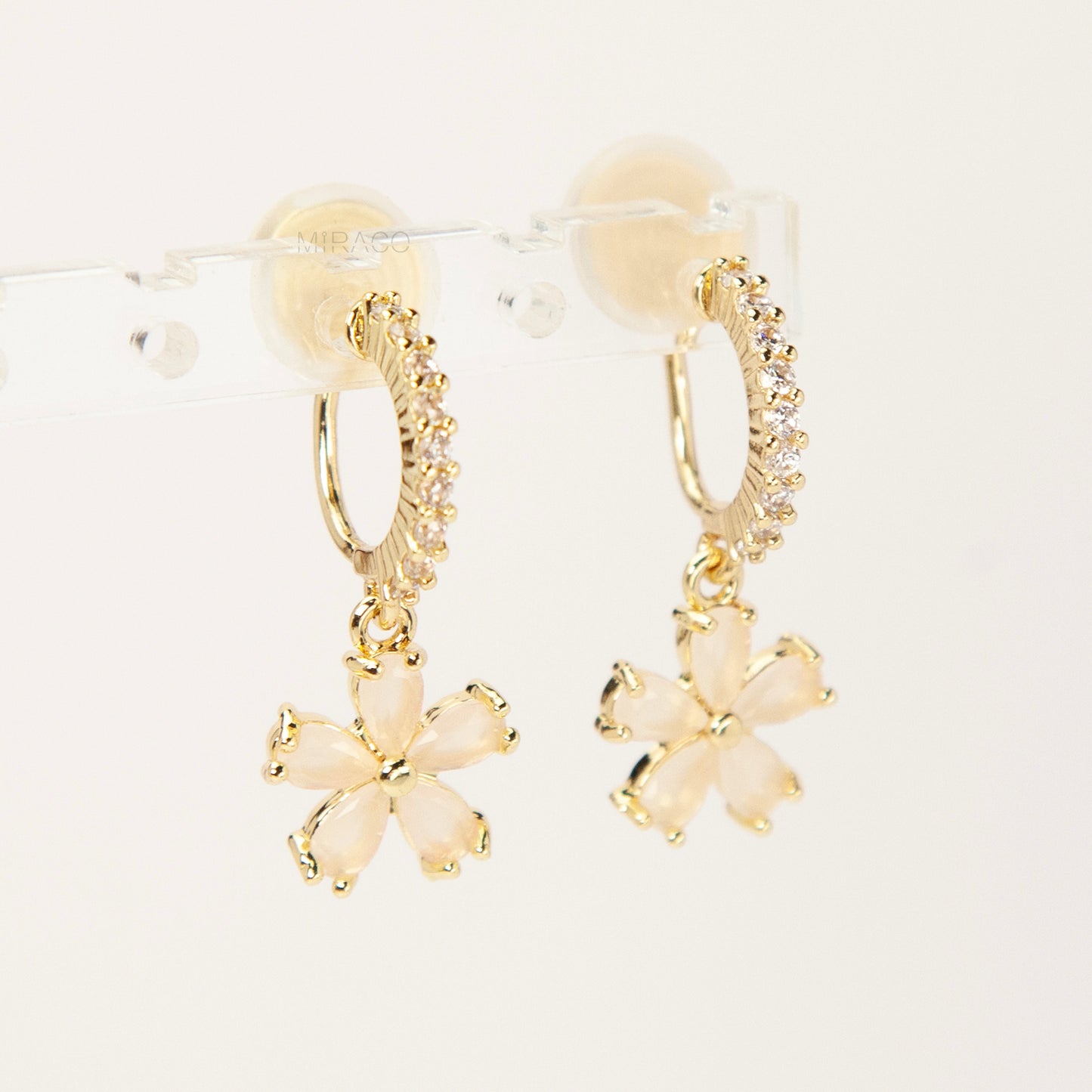 A pair of gold-tone drop clip-on earrings featuring a vertical bar set with small clear crystals and a dangling five-petal flower with opalescent stones, equipped with adjustable coil-spring backs.