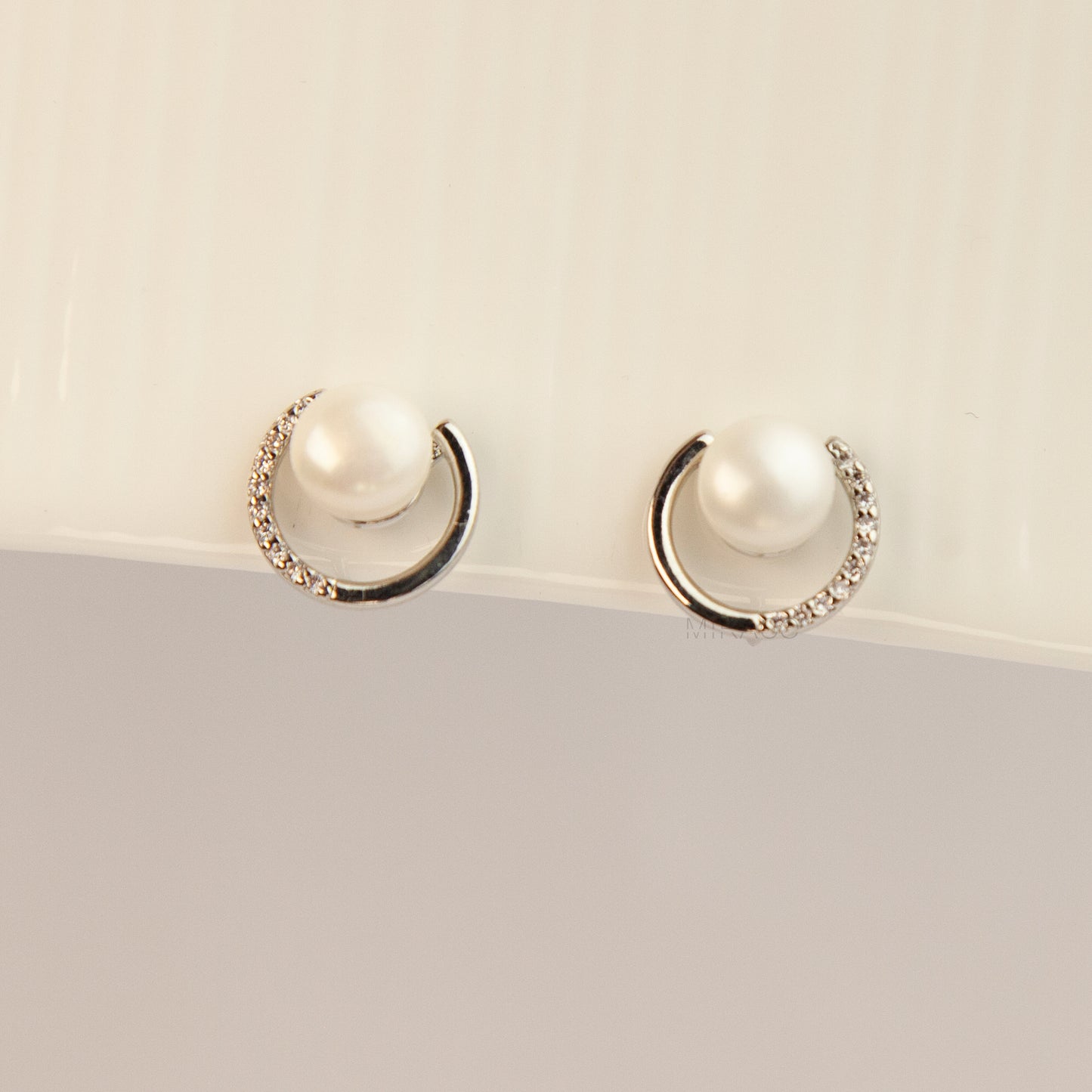 Pair of non-pierced silver-tone clip-on earrings with round silicone backs, featuring a real white freshwater pearl wrapped in a sparkling cubic zirconia crescent loop.