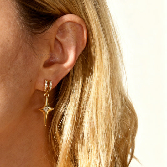 A pair of gold-toned dangle clip-on earrings featuring a modern, four-point North Star pendant centered with a clear rhinestone. The top closure is a comfortable coil-back style, partially covered with pave-set rhinestones.