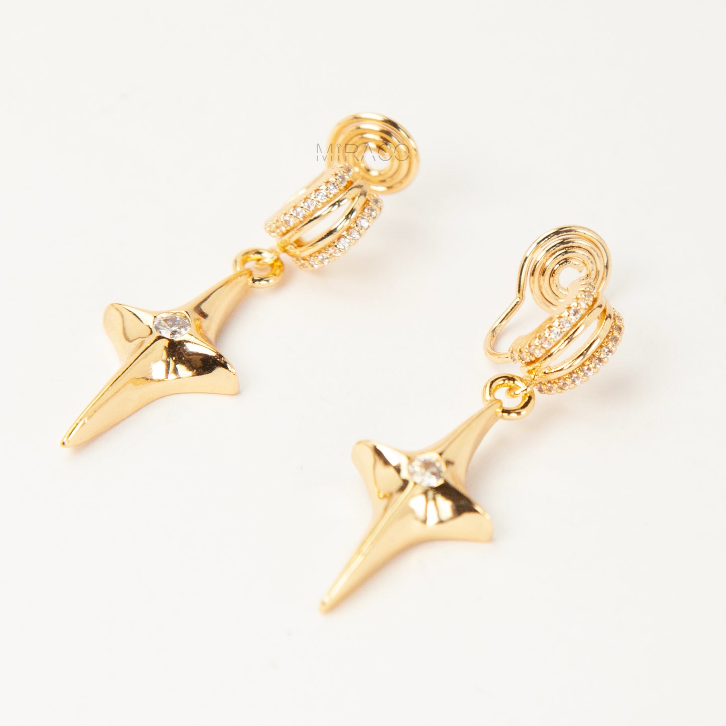 A pair of gold-toned dangle clip-on earrings featuring a modern, four-point North Star pendant centered with a clear rhinestone. The top closure is a comfortable coil-back style, partially covered with pave-set rhinestones.