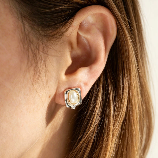 Close-up of an ear wearing a pearl stud earring with a neutral background