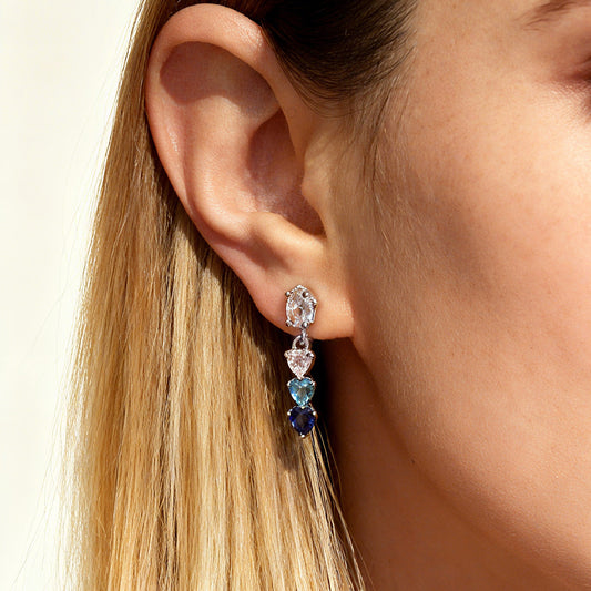 Close-up of an ear wearing a multi-colored gemstone earring, clip on earrings with heart-shaped gemstones, blue and white gem stone