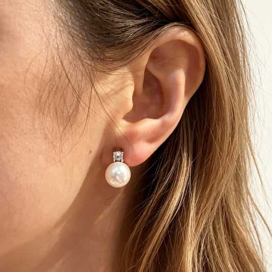 Woman wearing a silver-tone non-pierced clip-on earring featuring a round white pearl drop suspended from a sparkling cubic zirconia solitaire with a coil back.