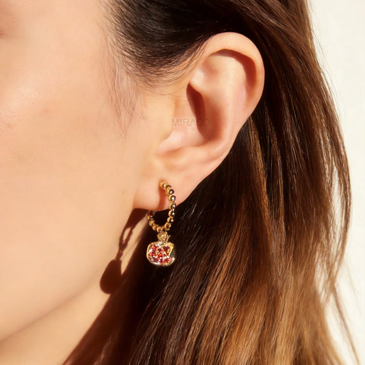 gold-tone clip-on earrings featuring a beaded drop design with a pomegranate charm filled with ruby red crystals, shown with comfortable coil backs.