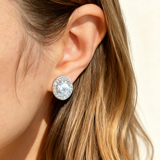 Pair of silver-tone oval halo clip-on stud earrings featuring a large central brilliant-cut cubic zirconia stone surrounded by a circle of small pave-set crystals.