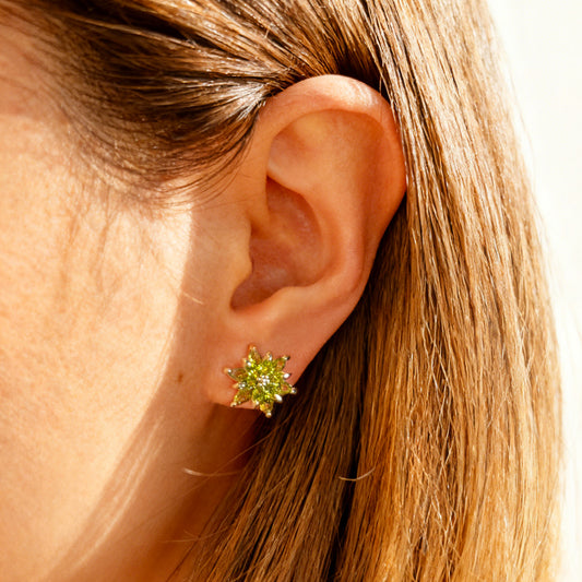 Pair of gold-tone clip-on earrings shaped like a flower or starburst, featuring marquise-cut peridot green crystals radiating from the center.