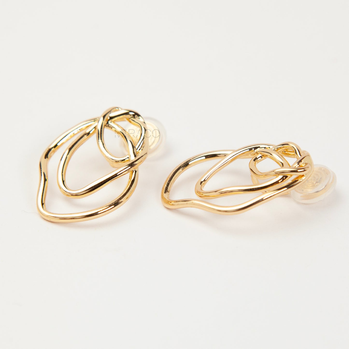 Close-up of comfortable gold-tone interlocking clip-on earrings featuring a modern, abstract double-ring design and a secure clear coil back closure. Non-pierced statement jewelry.