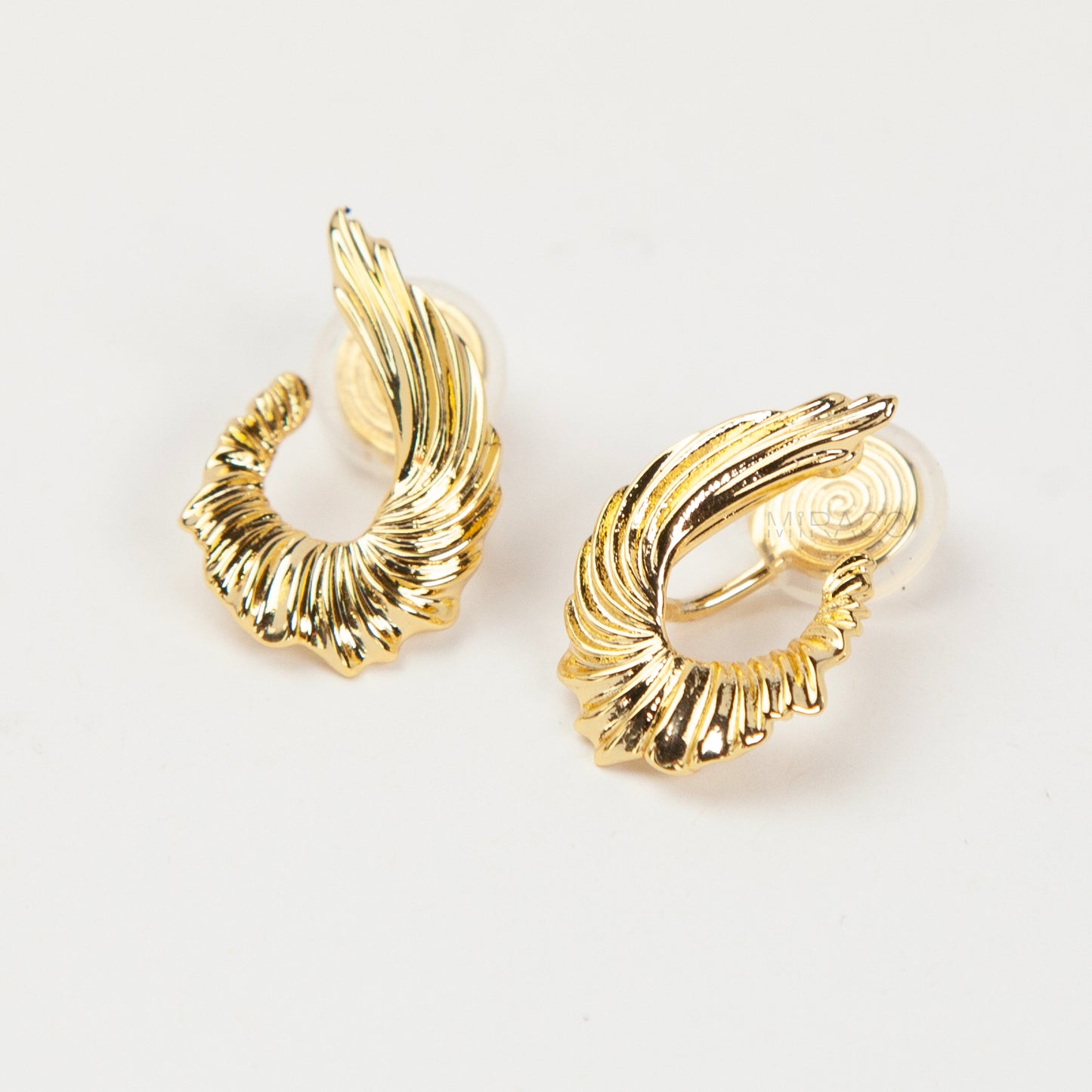 Close-up of comfortable gold-tone clip-on earrings with a ribbed, sculpted croissant or teardrop shape, worn on a model's ear. Features a secure coil back.