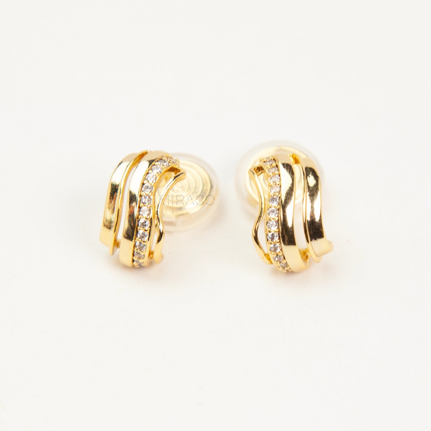 Close-up of gold-tone clip-on earrings featuring a modern stacked band design with a row of small clear crystals and a spiral coil-back.