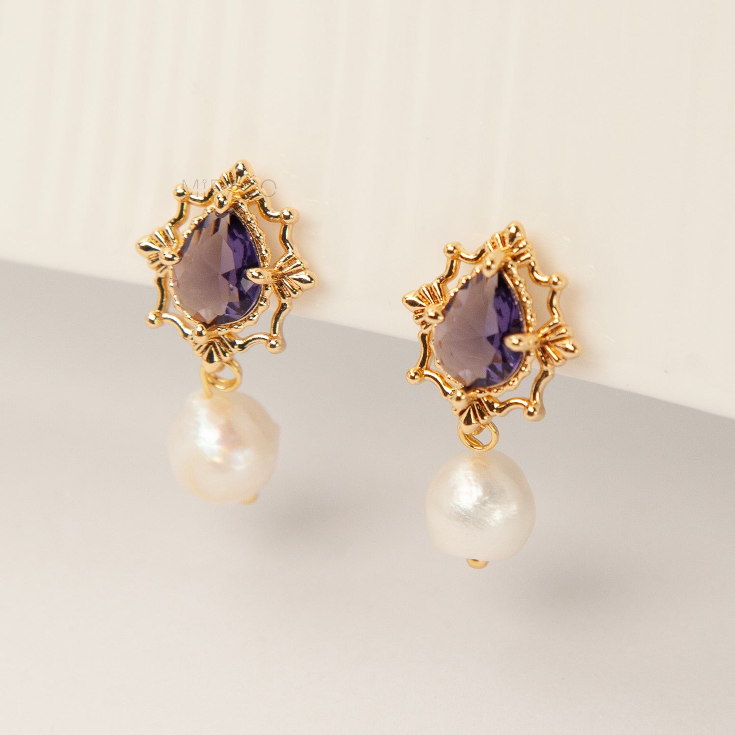 Pair of gold-plated, coil-back clip-on earrings with an ornate Victorian-style setting holding a purple pear-cut gemstone (amethyst color) and a dangling real baroque freshwater pearl.