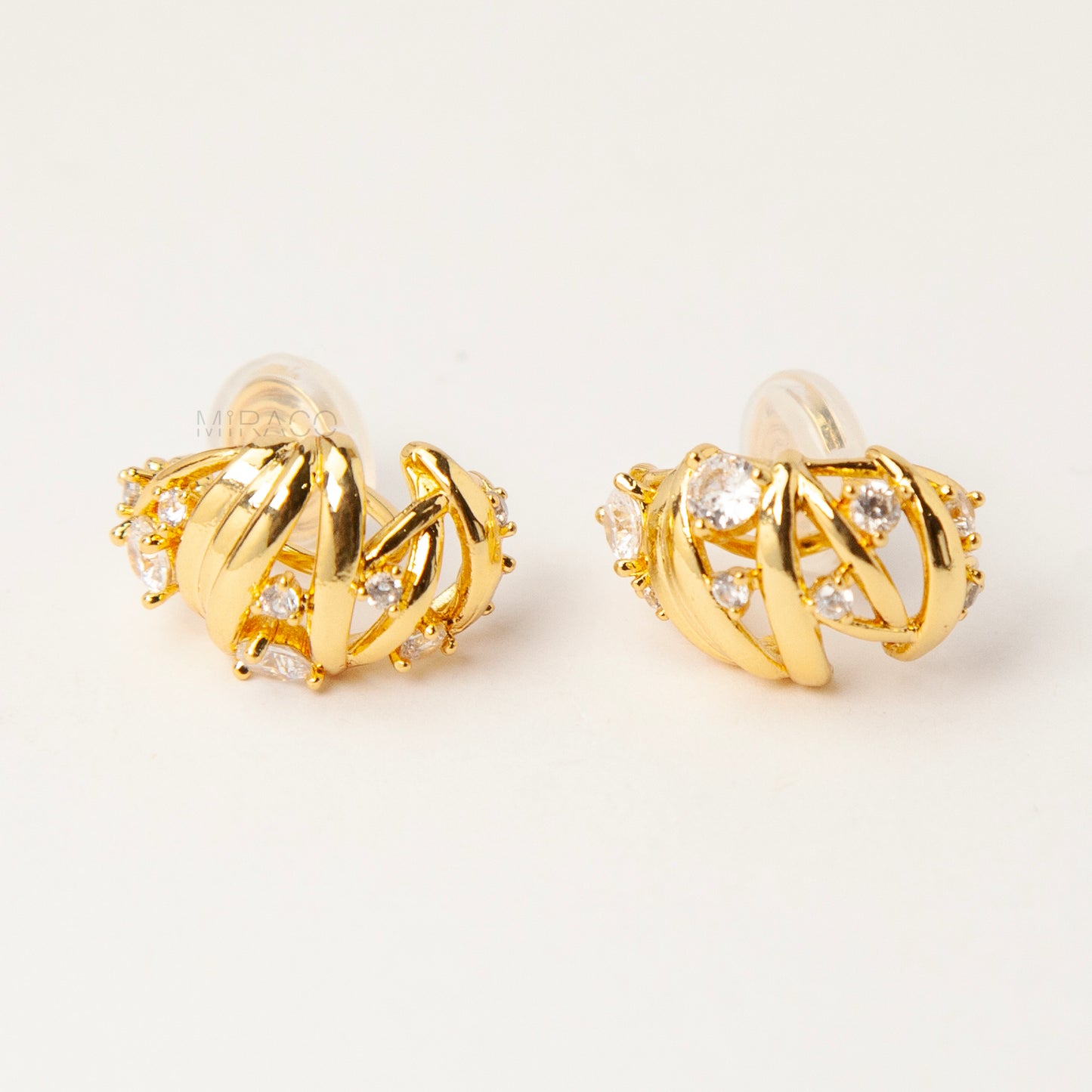 Gold clip-on earrings with wrapped sculptural design and clear crystal accents, featuring a comfortable coil back for non-pierced ears