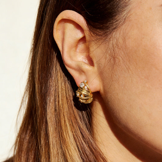 Gold clip-on earrings with wrapped sculptural design and clear crystal accents, featuring a comfortable coil back for non-pierced ears