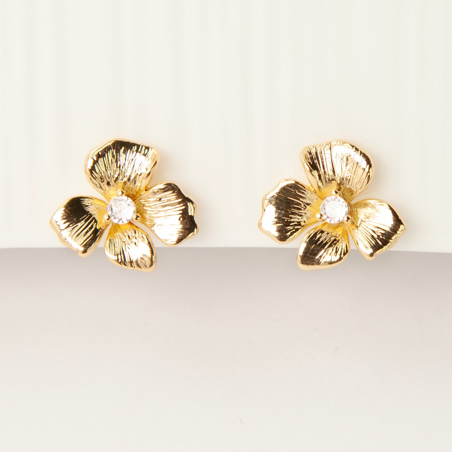 Pair of gold-tone textured flower-shaped clip-on earrings with a round clear crystal center and comfortable coil-back closures on a white background.