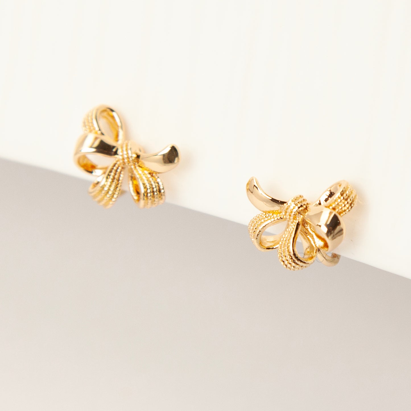 Pair of gold-tone multi-loop bow ribbon clip-on earrings featuring textured detailing and comfortable coil-back closures with clear silicone pads.