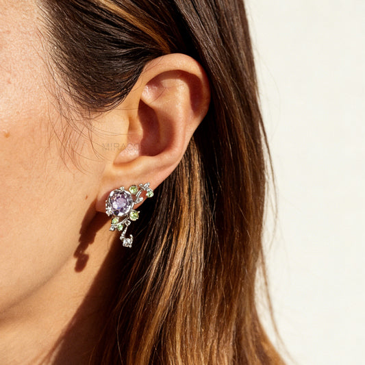 Pair of silver-tone floral clip-on earrings featuring a lavender center crystal, green leaf accents, and comfortable invisible coil back closures.