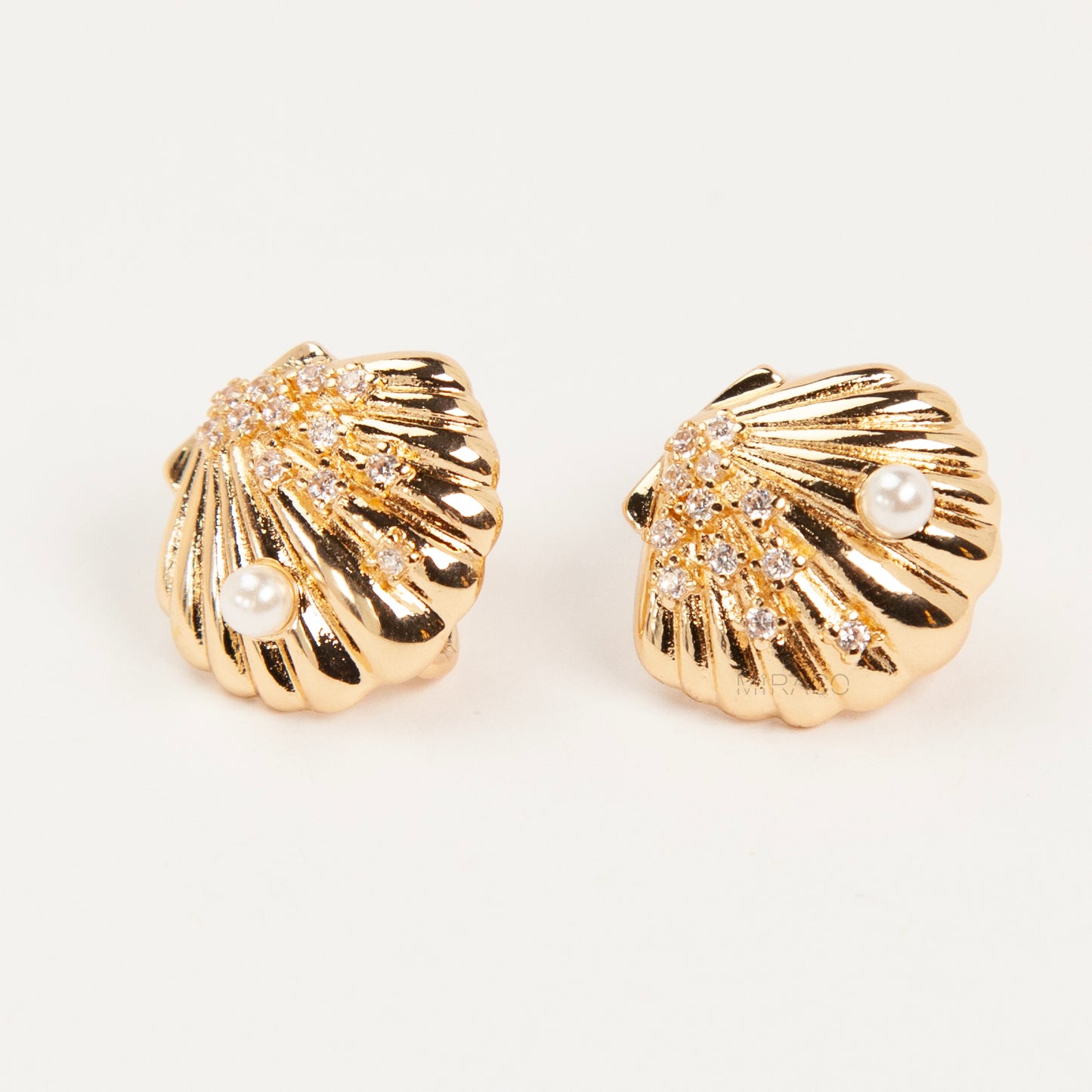 Pair of gold-tone scalloped seashell clip-on earrings featuring a small pearl and pavé crystals with comfortable invisible coil back closures.