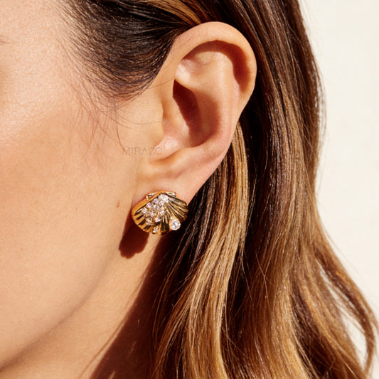 Pair of gold-tone scalloped seashell clip-on earrings featuring a small pearl and pavé crystals with comfortable invisible coil back closures.