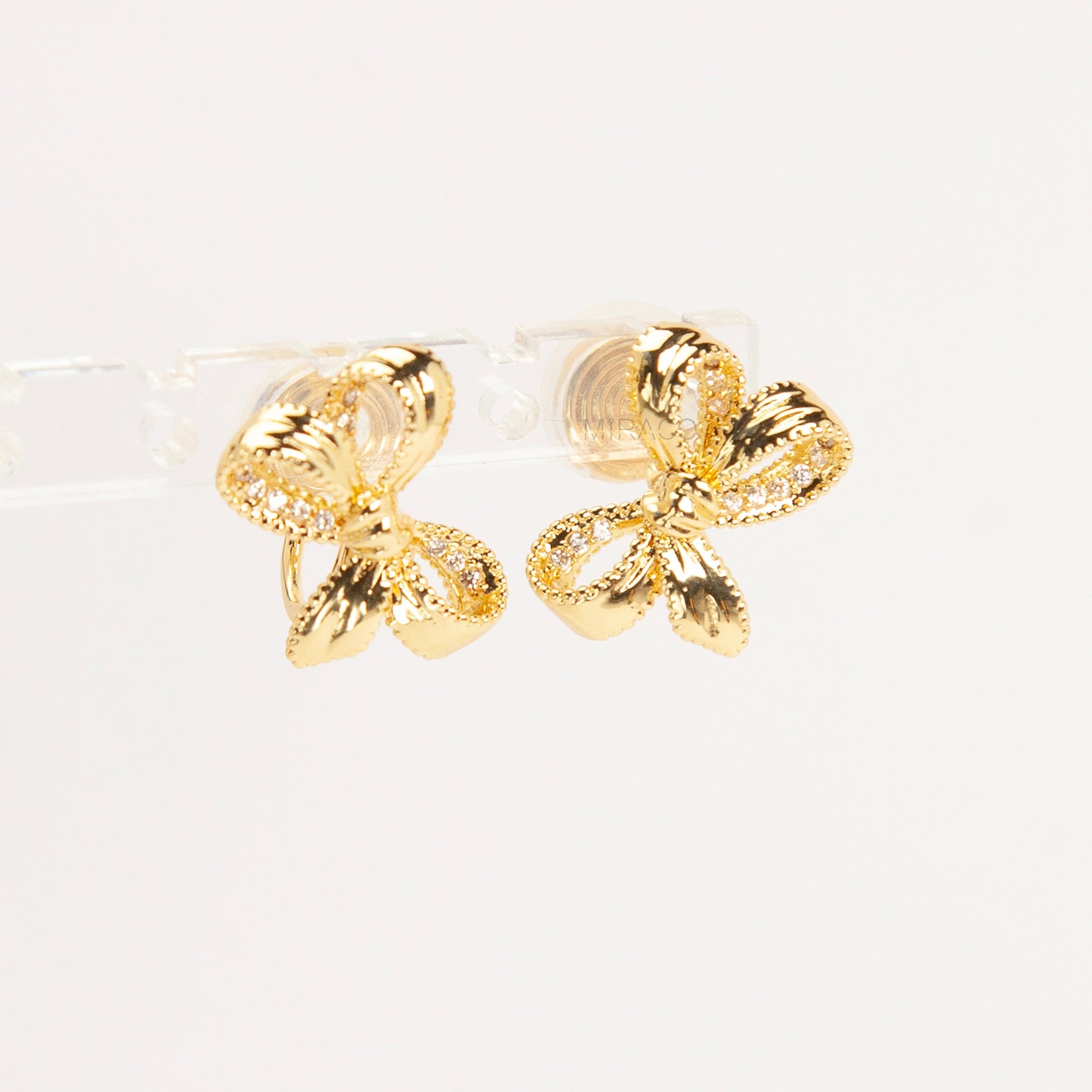 Pair of dainty gold-toned ribbon bow clip-on earrings with pave crystal details and a comfortable silver-tone coil back mechanism for non-pierced ears.
