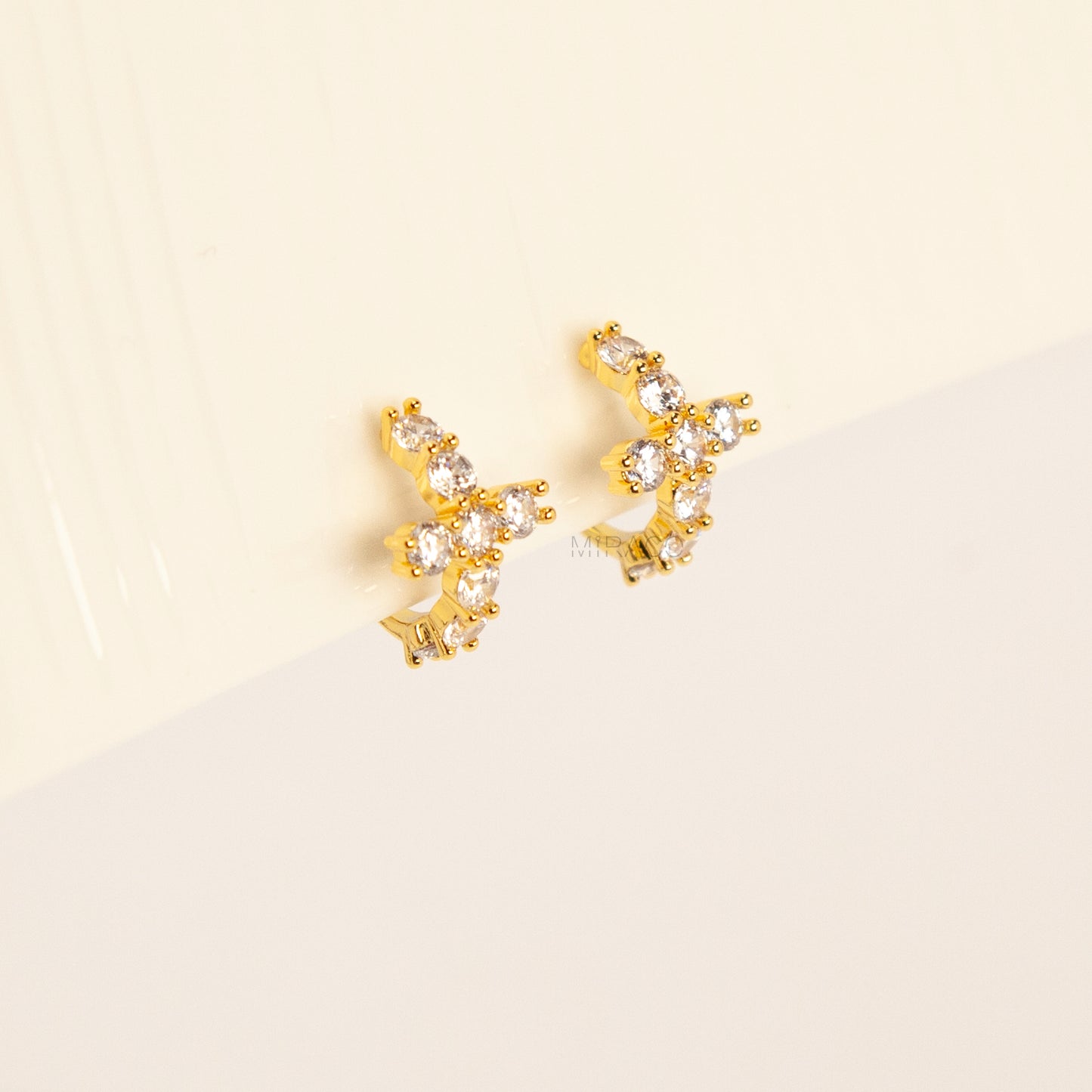 A pair of gold-tone clip-on hoop earrings shaped like crosses, embellished with clear round crystals and featuring translucent round silicone comfort pads on the back.