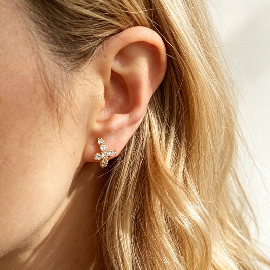 A pair of gold-tone clip-on hoop earrings shaped like crosses, embellished with clear round crystals and featuring translucent round silicone comfort pads on the back.