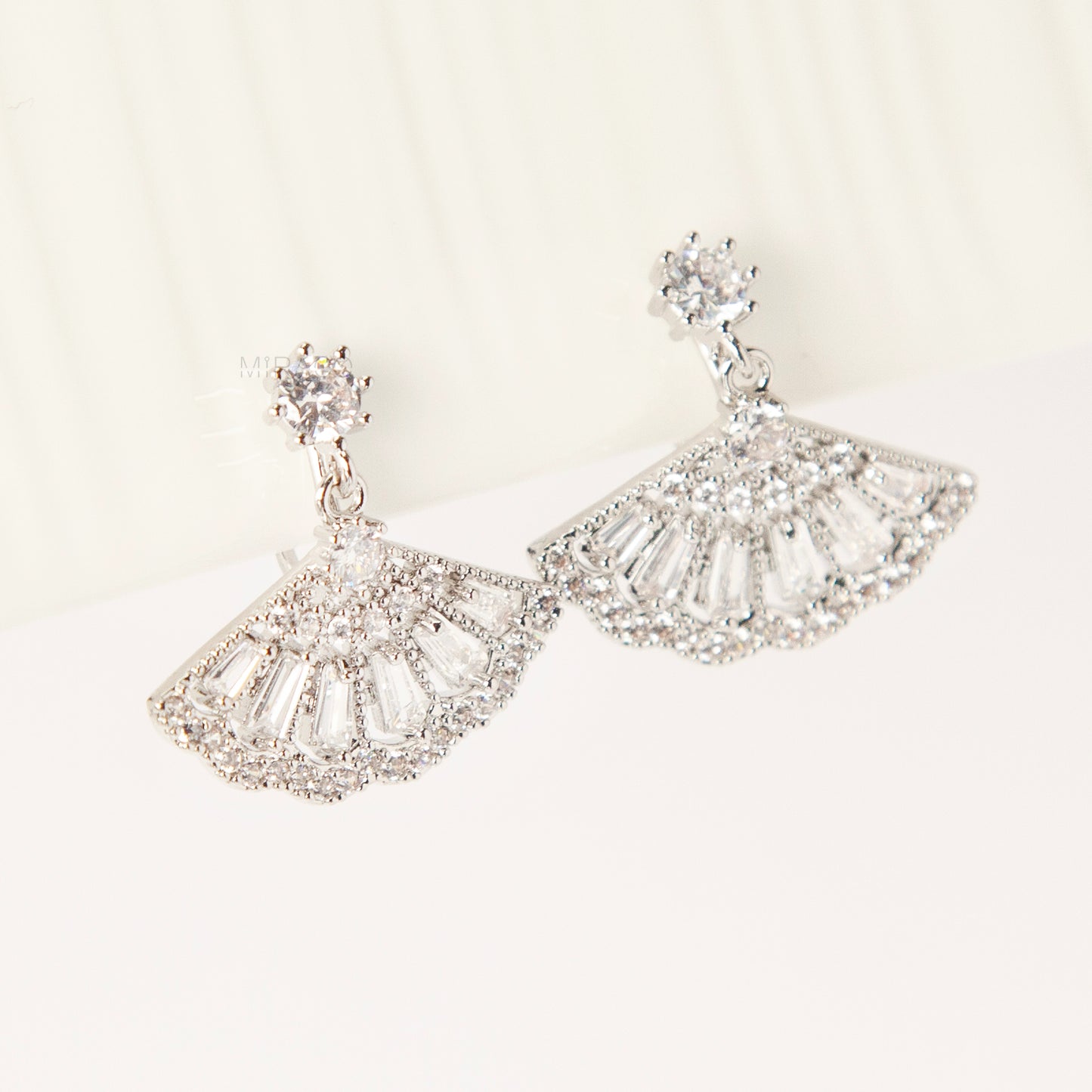 A pair of silver-tone Art Deco style clip-on drop earrings featuring a fan-shaped design set with baguette and round clear crystals, with adjustable coil-spring backs.