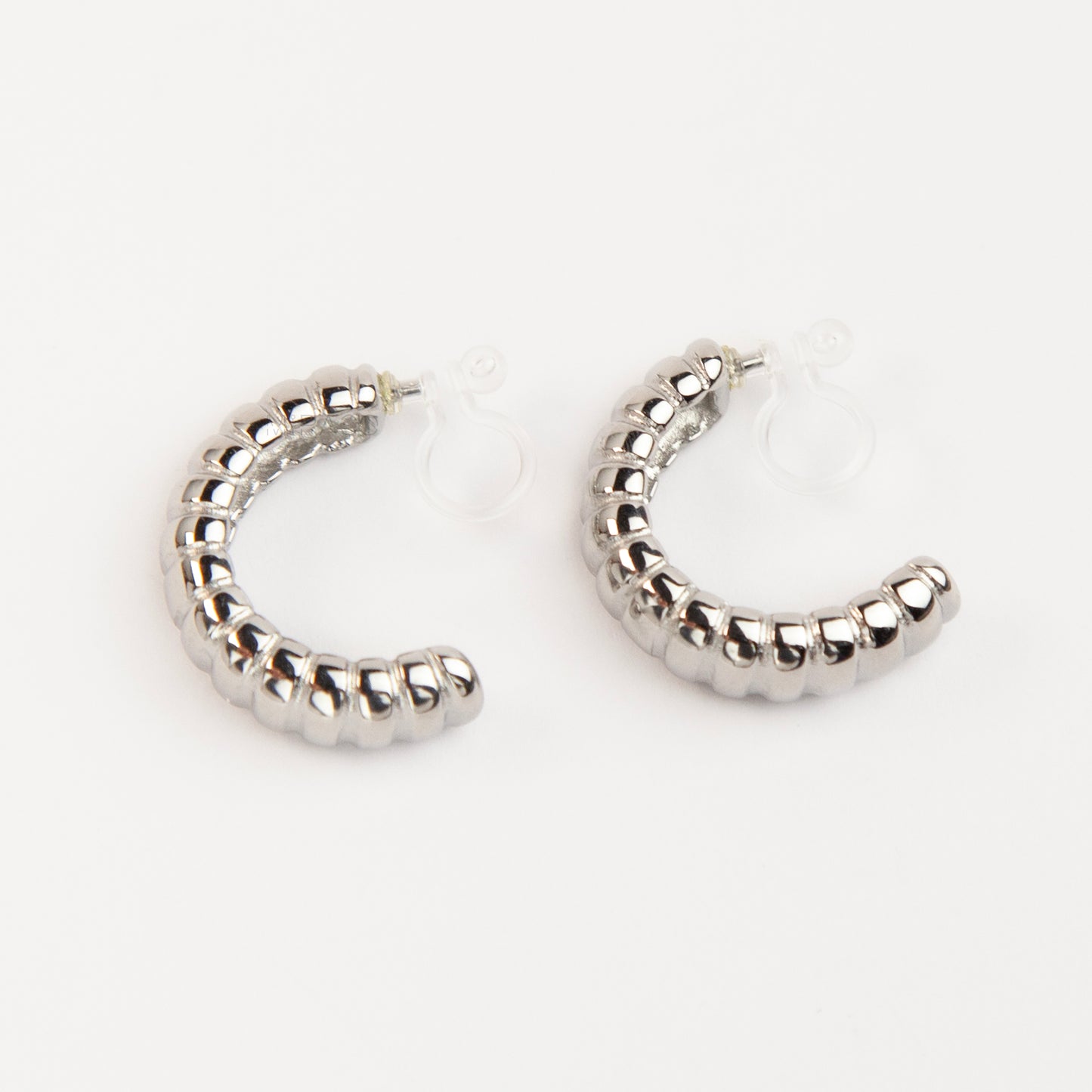 Two pairs of textured croissant-style C-hoop earrings, one pair in gold and one pair in silver, featuring clear invisible resin clip-on backs