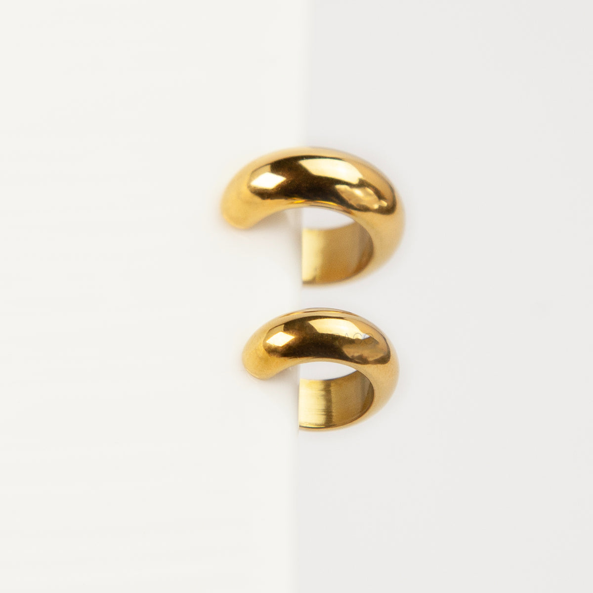 Two chunky, polished gold-tone stainless steel ear cuffs with a smooth, rounded dome design, displayed side-by-side in different sizes on a white background.