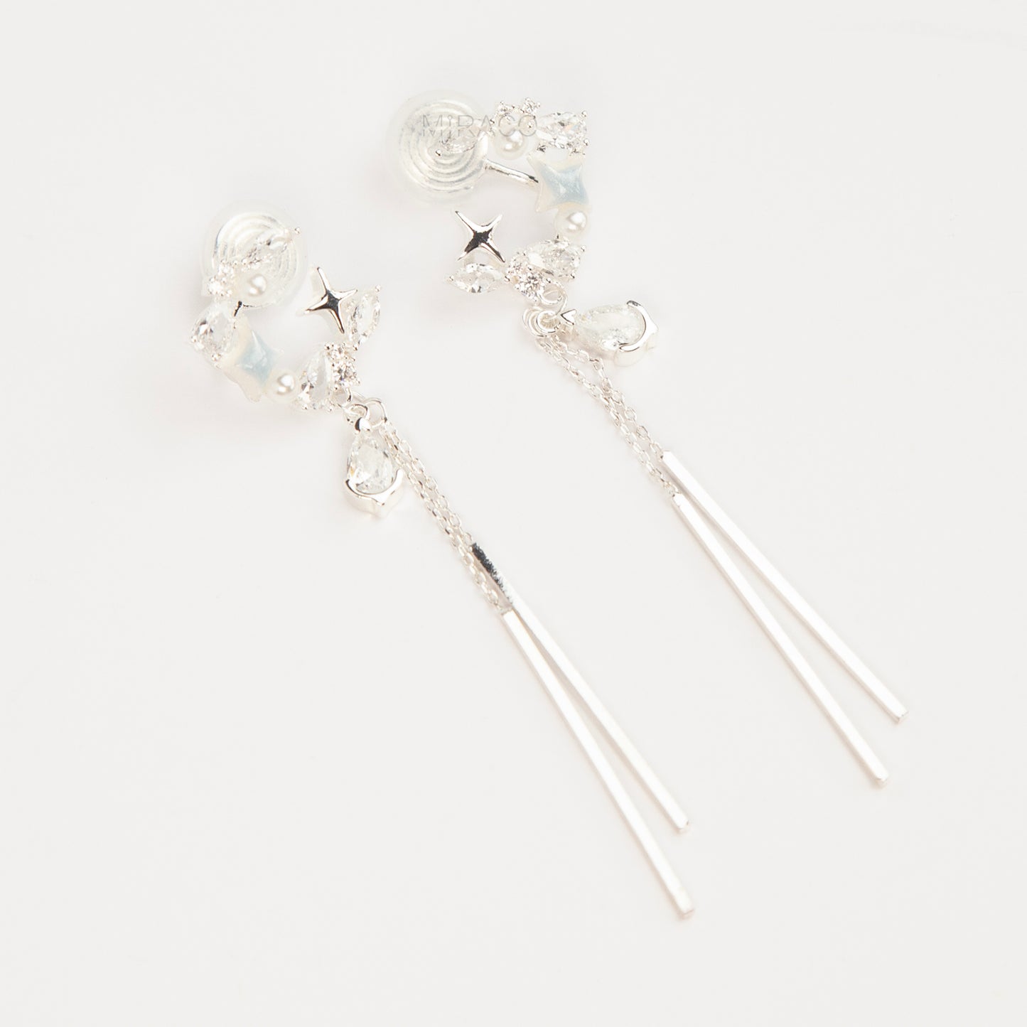 A pair of elegant silver celestial dangle clip-on earrings, featuring a crescent moon and star design accented with marquise crystals and tiny pearls, cascading into a teardrop gemstone and sleek, vertical metallic bar tassels on comfortable coil backs.
