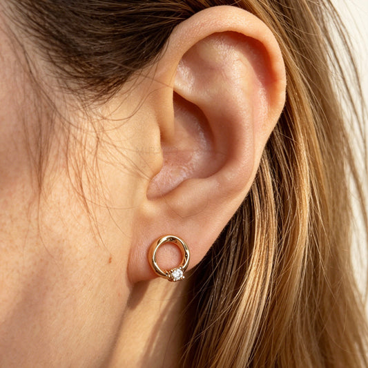 A pair of gold open circle stud clip-on earrings accented with a single sparkling round crystal and fitted with comfortable coil backs with clear silicone cushions.
