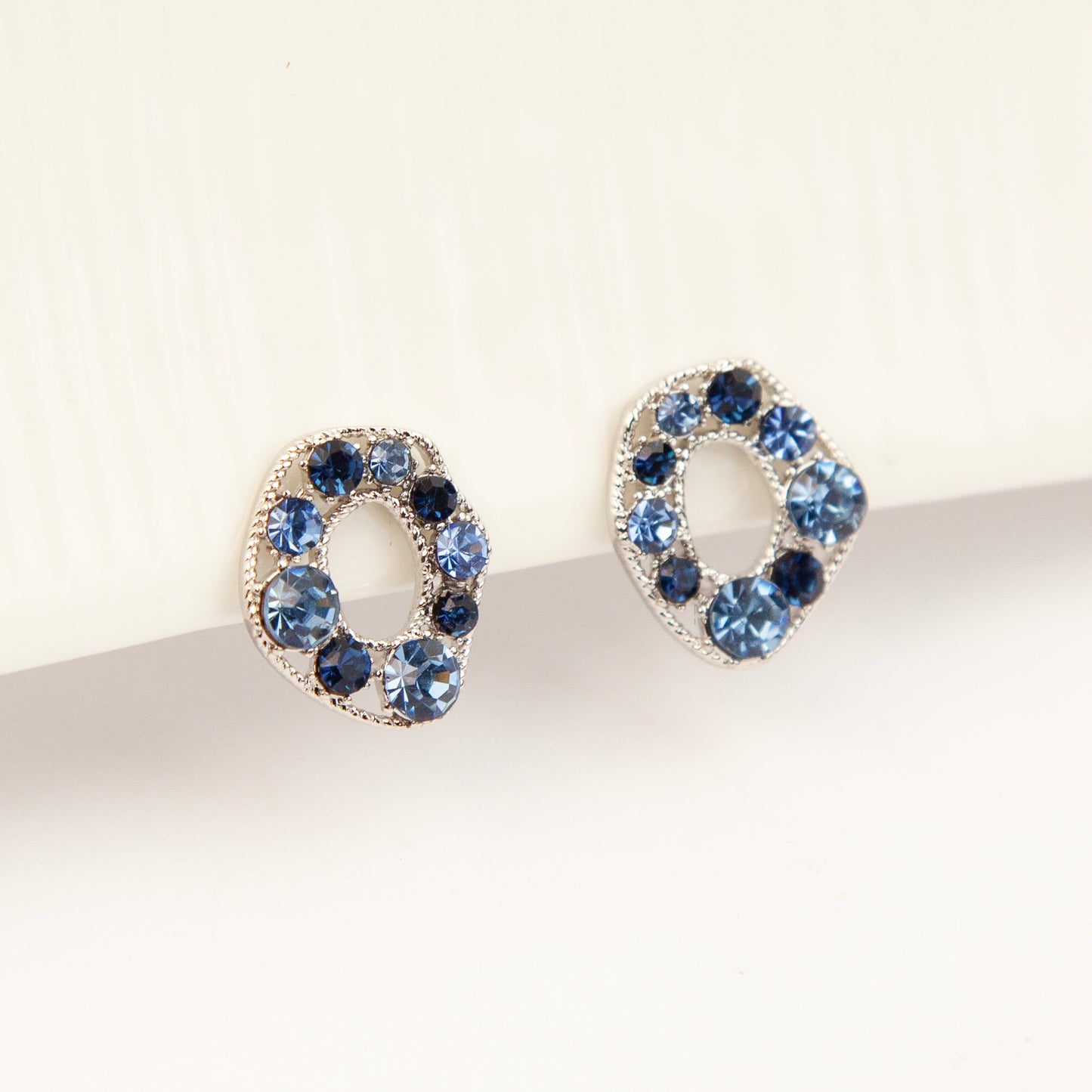Pair of oval silver-tone non-pierced clip-on earrings with coil backs, set with sparkling dark and light blue crystals.