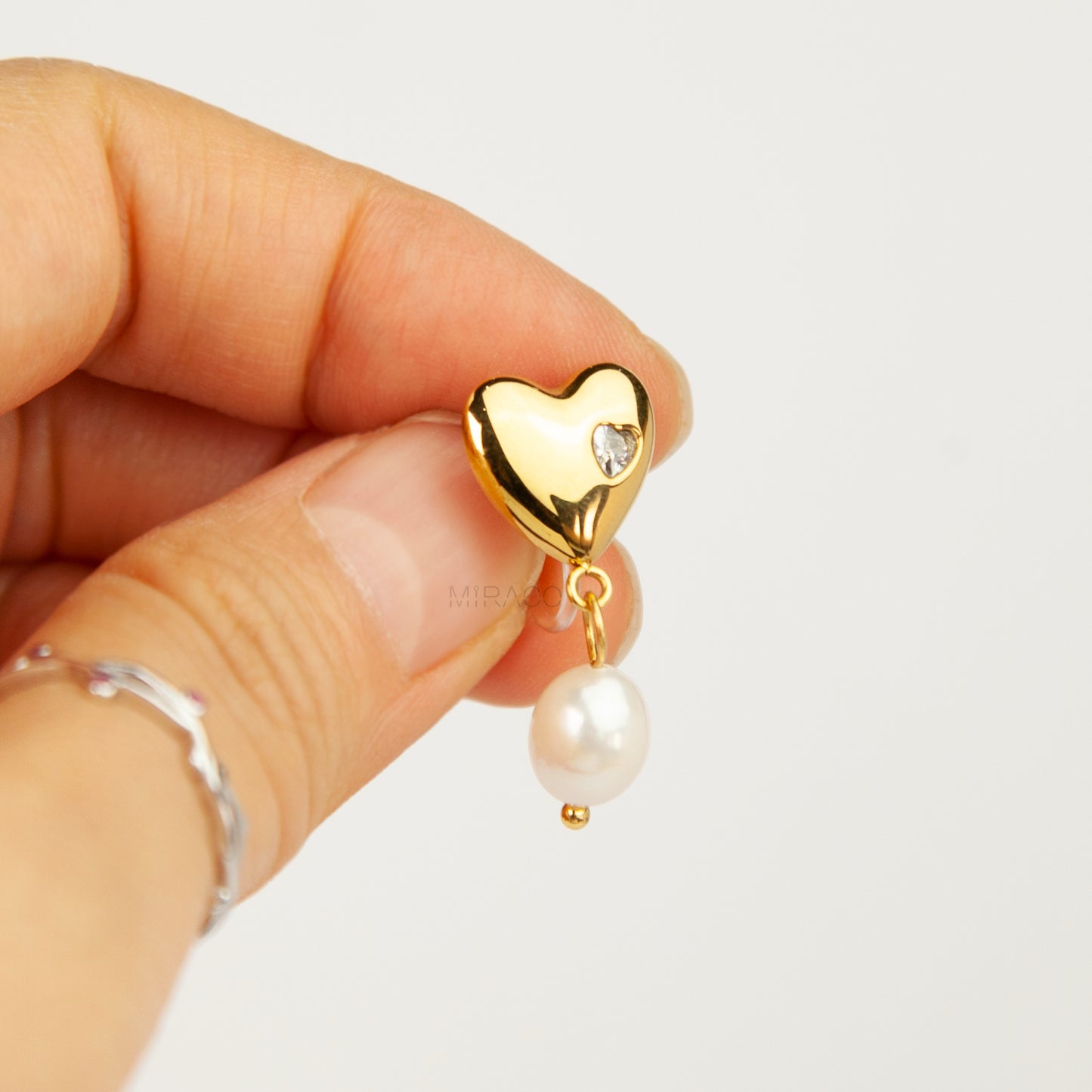 Pair of polished gold puffy heart clip-on earrings with star-set cz detail and dangling white pearls featuring clear invisible resin backs for non-pierced ears against a white backdrop.