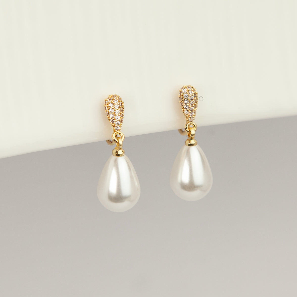 Gold coil-back clip-on drop earrings featuring a pave crystal teardrop stud and dangling white pear-shaped pearl