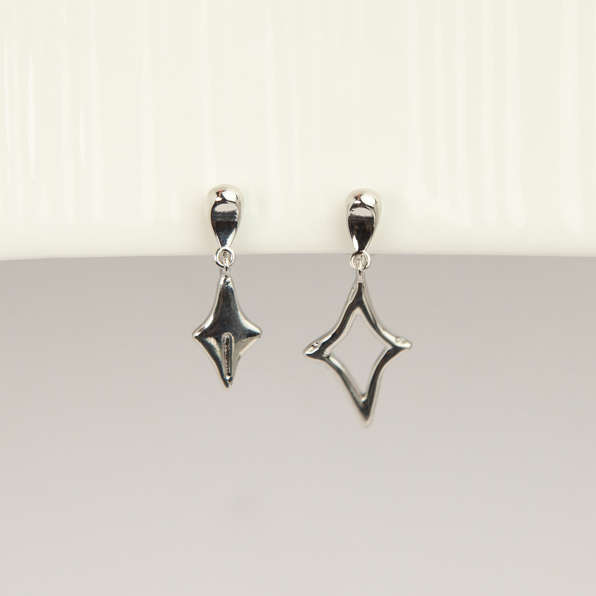Silver coil-back clip-on drop earrings featuring mismatched solid and hollow four-point starburst charms