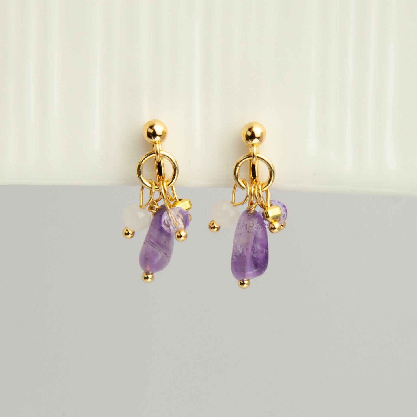 Gold screw-back clip-on hoop earrings with a raw purple amethyst stone, faceted lilac crystal charm, and white bead displayed on a light background.