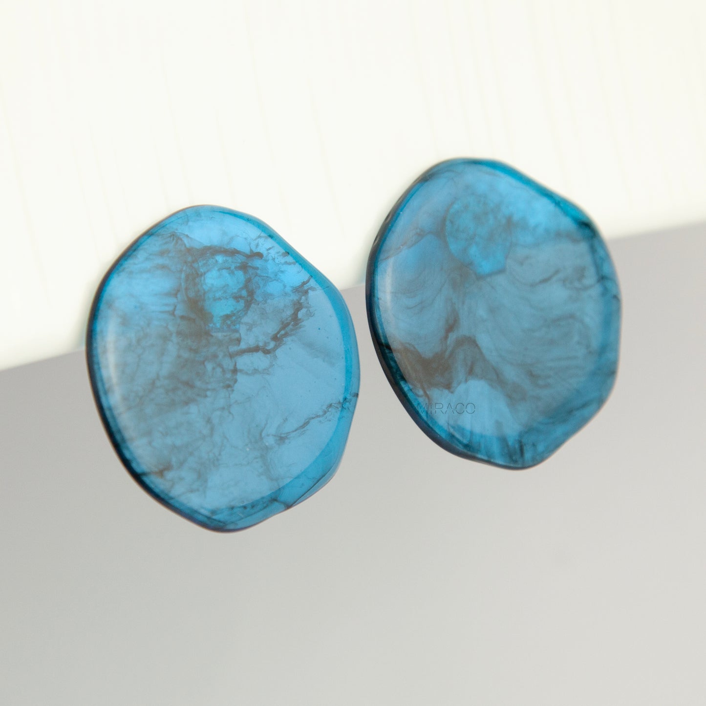 Large organic oval clip-on earring featuring a blue and black marbled resin design