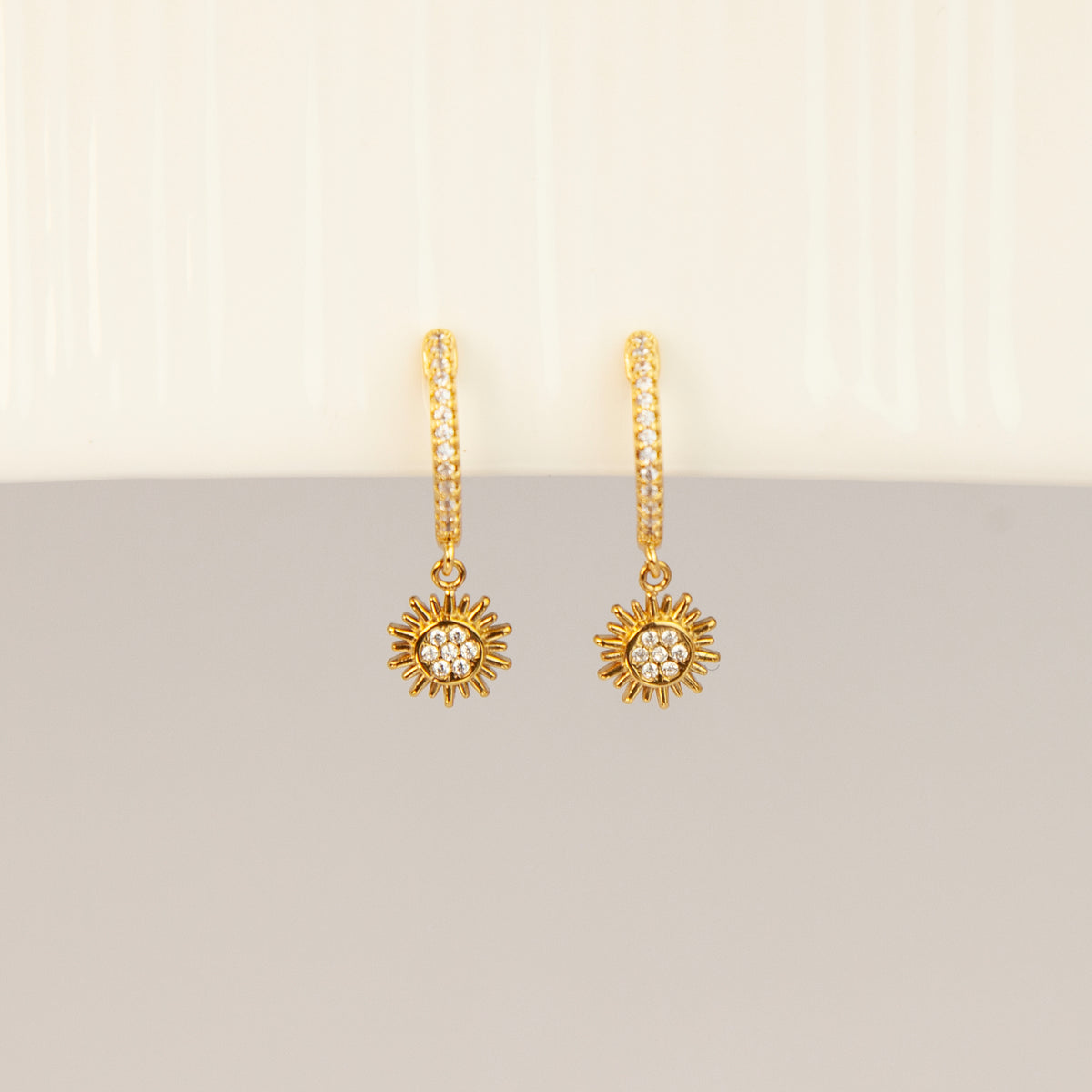 Gold clip-on hoop earrings with pave cubic zirconia pavé detailing, dangling celestial sunburst charms, and clear round silicone comfort backings.