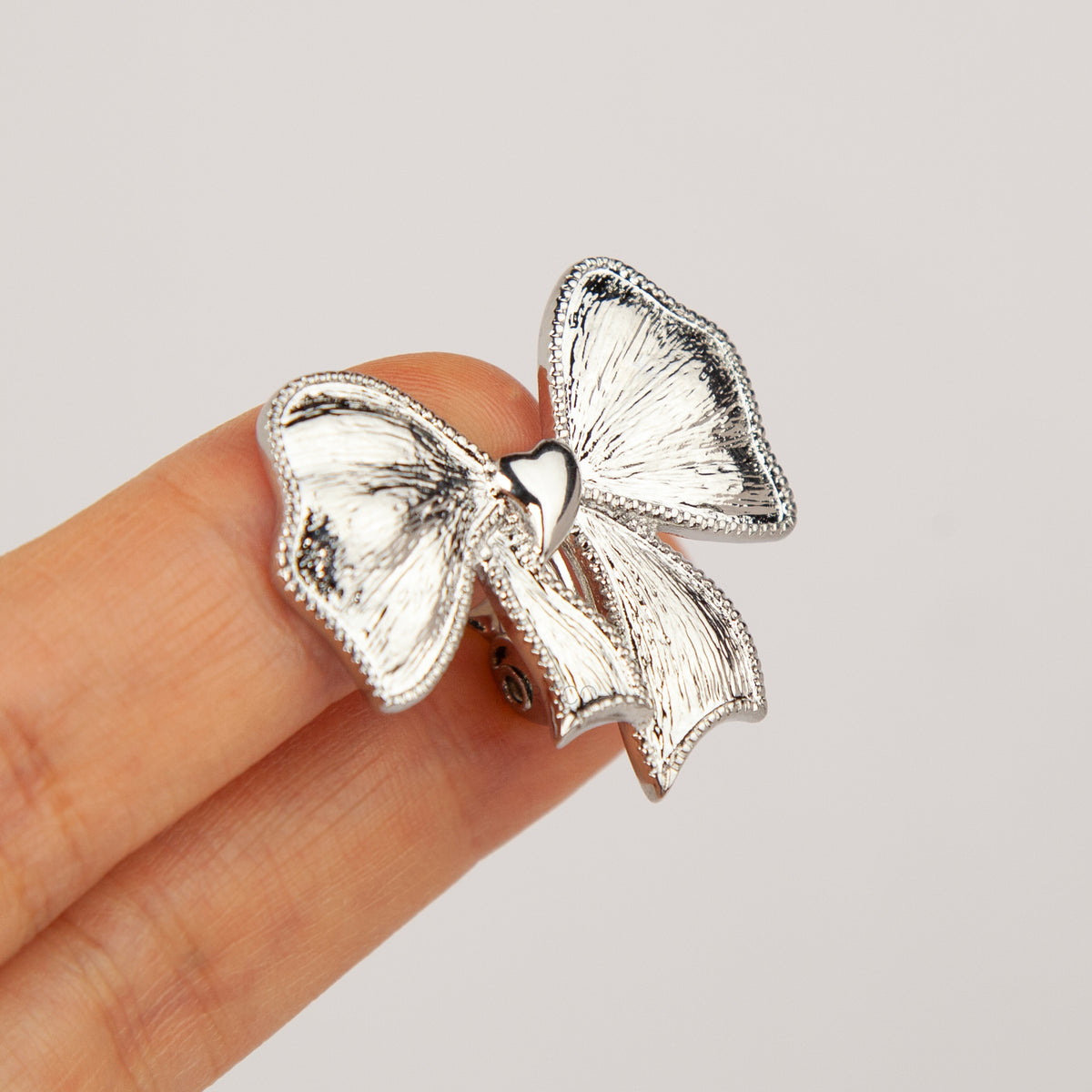 Woman wearing textured silver ribbon bow clip-on earring with a comfortable foldable paddle back for non-pierced ears.