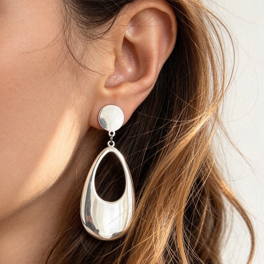 Woman wearing bold silver stainless steel hollow teardrop clip-on dangle earrings with discreet mini-clip backs for non-pierced ears.