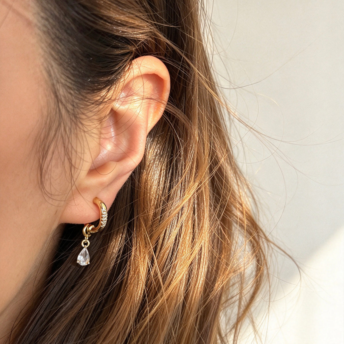 Gold and silver huggie clip-on hoop earrings with pavé cubic zirconia and teardrop CZ drop pendants featuring coil backs for non-pierced ears.