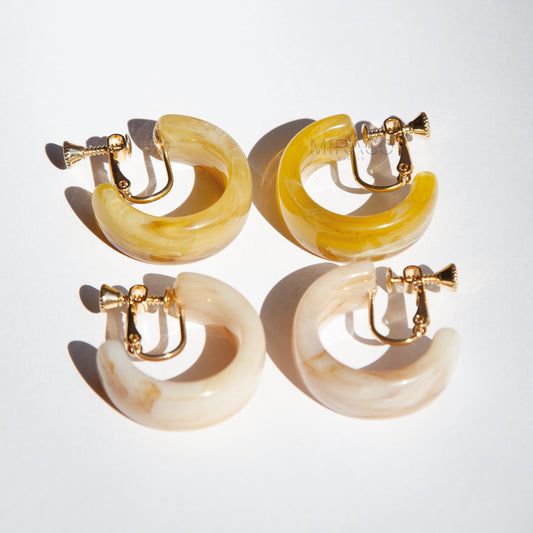 Classic Hoops, Modern Comfort – No Piercing Required! Get the timeless appeal of hoop earrings with the ultimate convenience of clip-ons! These eye-catching hoops are crafted from beautifully marbled resin, featuring unique swirls of color that add a touch of artistic flair to any outfit. Available in two chic colorways –&nbsp;Amber Swirl and&nbsp;Cream Swirl – they offer versatile style options.
