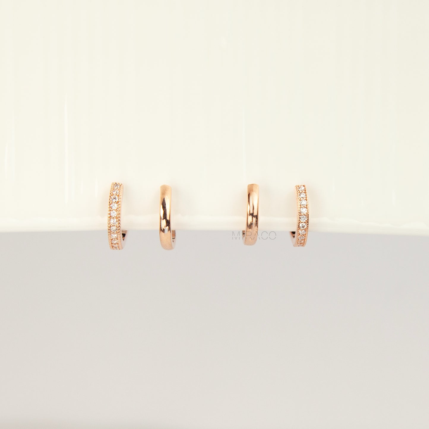 Pair of rose gold non-pierced double band clip-on hoop earrings with pavé cubic zirconia accents and clear silicone spiral coil backs.