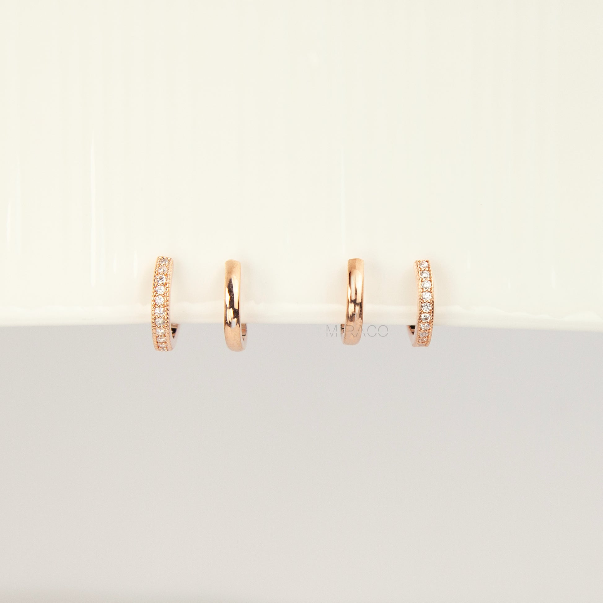 Pair of rose gold non-pierced double band clip-on hoop earrings with pavé cubic zirconia accents and clear silicone spiral coil backs.
