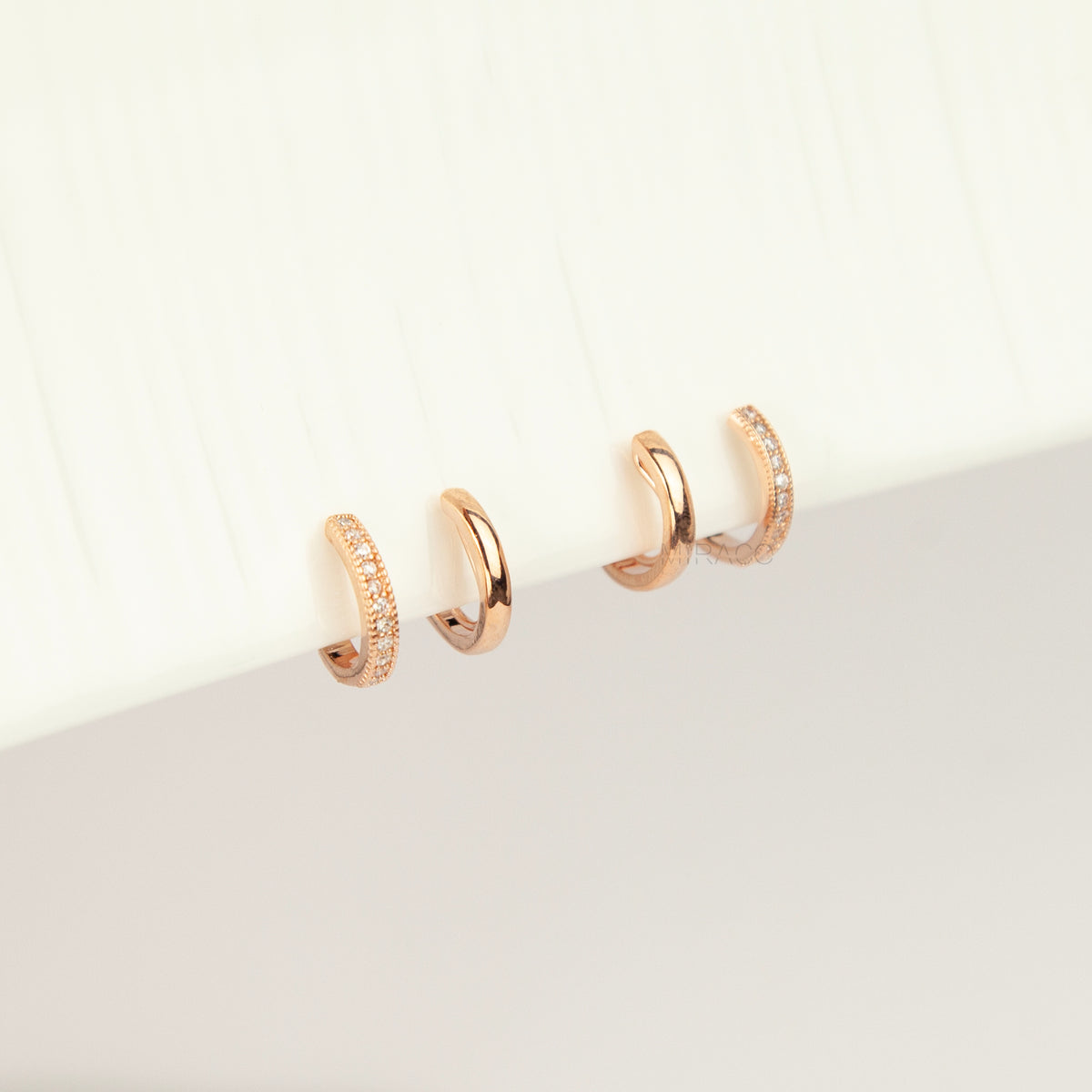 Pair of rose gold non-pierced double band clip-on hoop earrings with pavé cubic zirconia accents and clear silicone spiral coil backs.