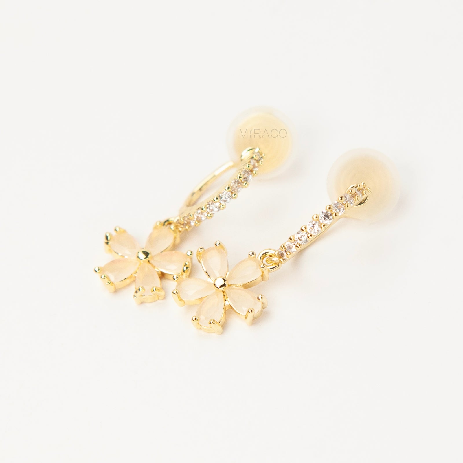 A pair of gold-tone drop clip-on earrings featuring a vertical bar set with small clear crystals and a dangling five-petal flower with opalescent stones, equipped with adjustable coil-spring backs.