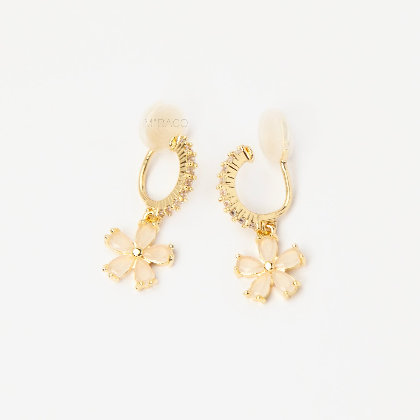 A pair of gold-tone drop clip-on earrings featuring a vertical bar set with small clear crystals and a dangling five-petal flower with opalescent stones, equipped with adjustable coil-spring backs.