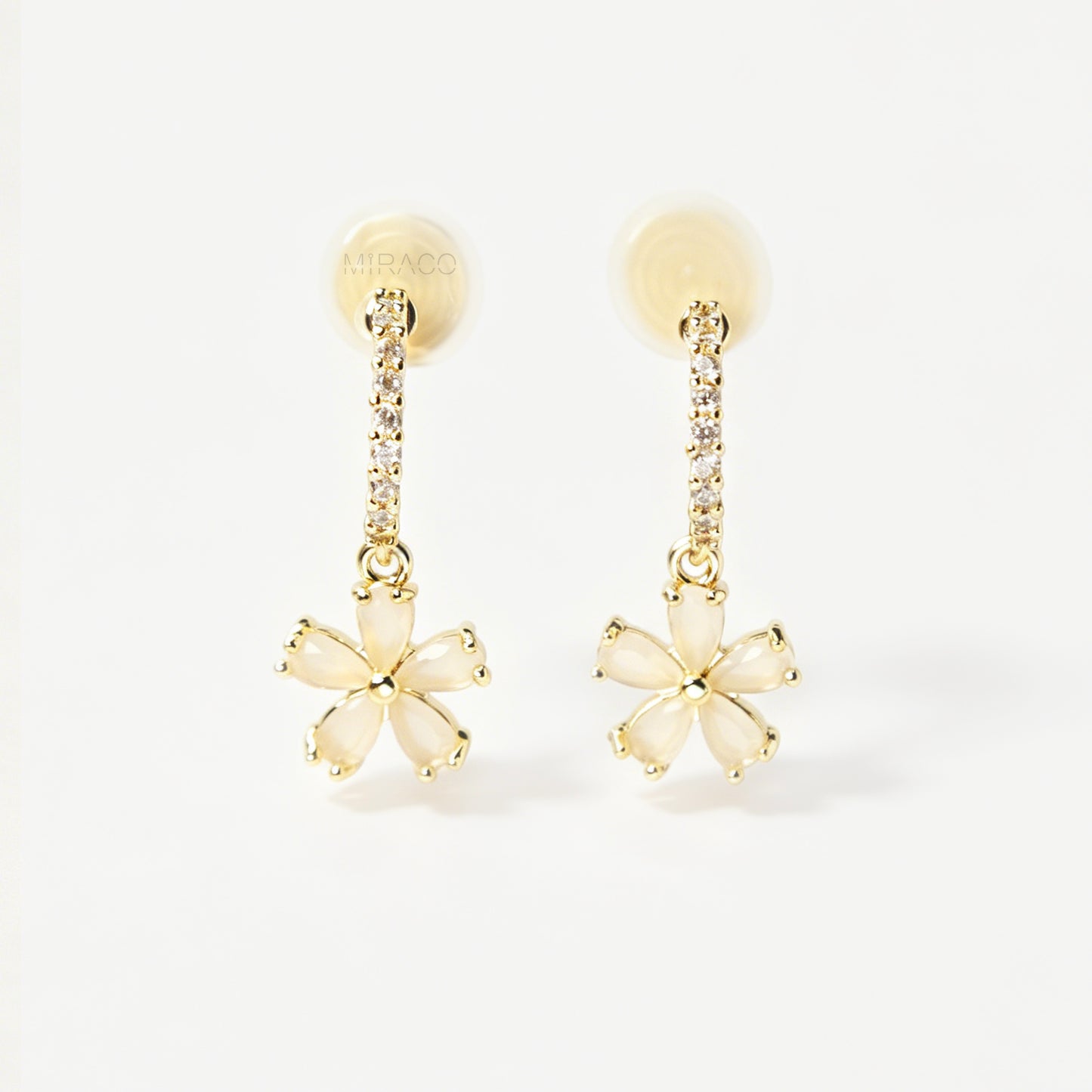 A pair of gold-tone drop clip-on earrings featuring a vertical bar set with small clear crystals and a dangling five-petal flower with opalescent stones, equipped with adjustable coil-spring backs.