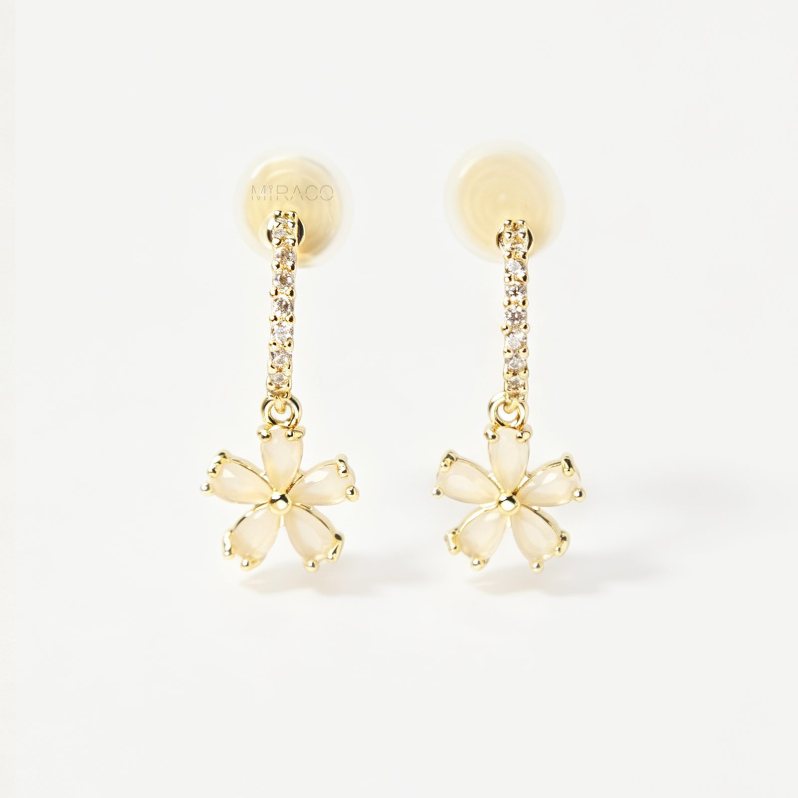 A pair of gold-tone drop clip-on earrings featuring a vertical bar set with small clear crystals and a dangling five-petal flower with opalescent stones, equipped with adjustable coil-spring backs.