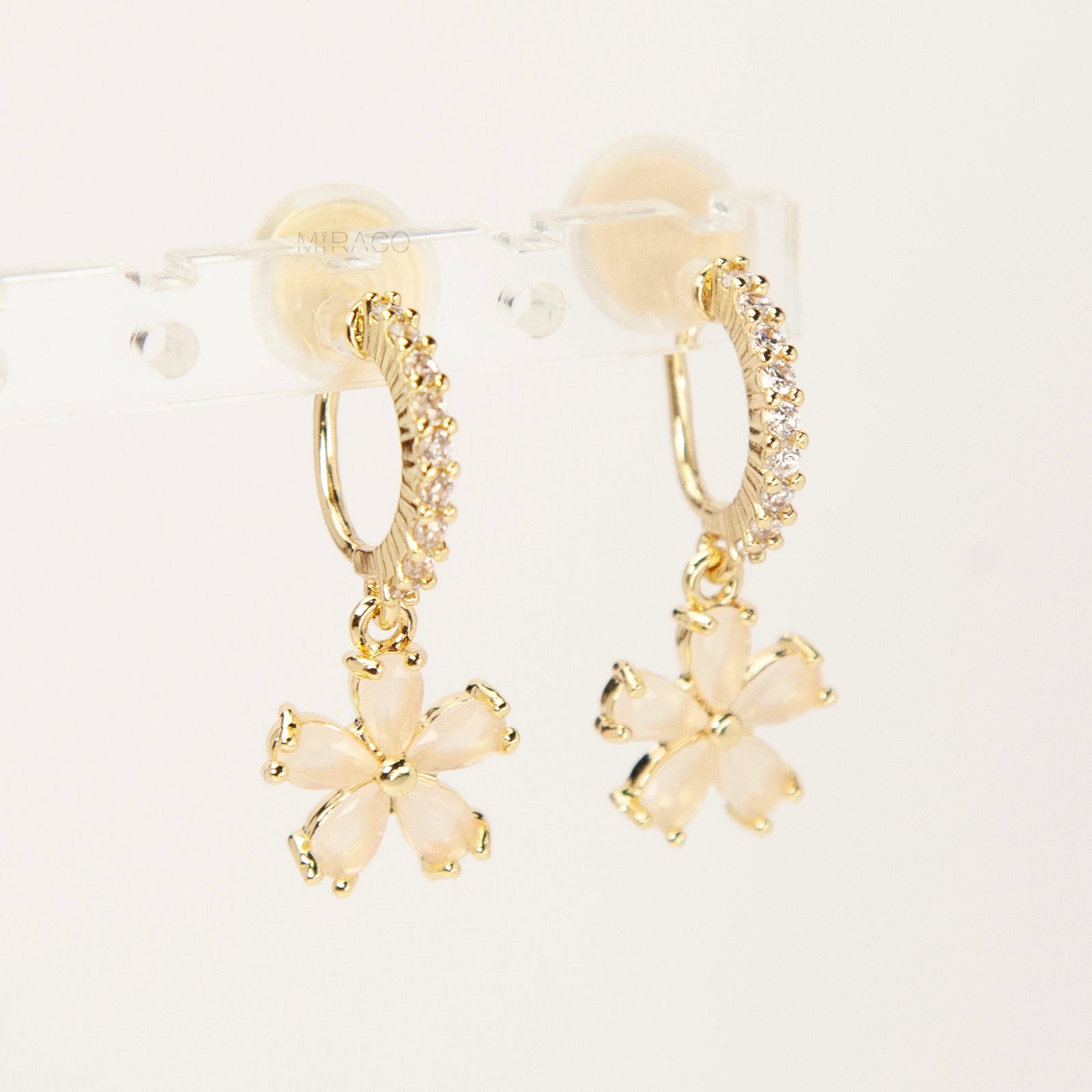 A pair of gold-tone drop clip-on earrings featuring a vertical bar set with small clear crystals and a dangling five-petal flower with opalescent stones, equipped with adjustable coil-spring backs.