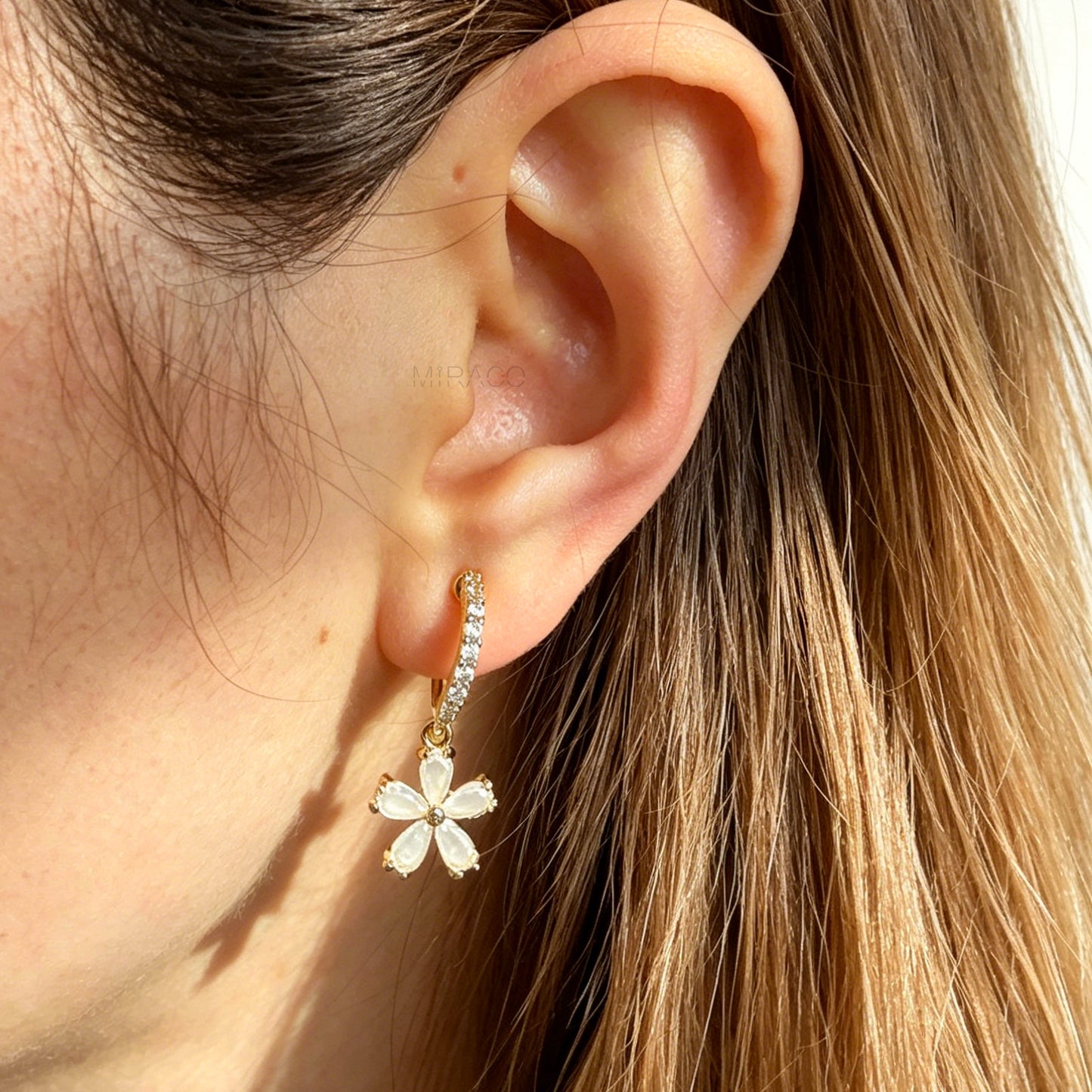 A pair of gold-tone drop clip-on earrings featuring a vertical bar set with small clear crystals and a dangling five-petal flower with opalescent stones, equipped with adjustable coil-spring backs.