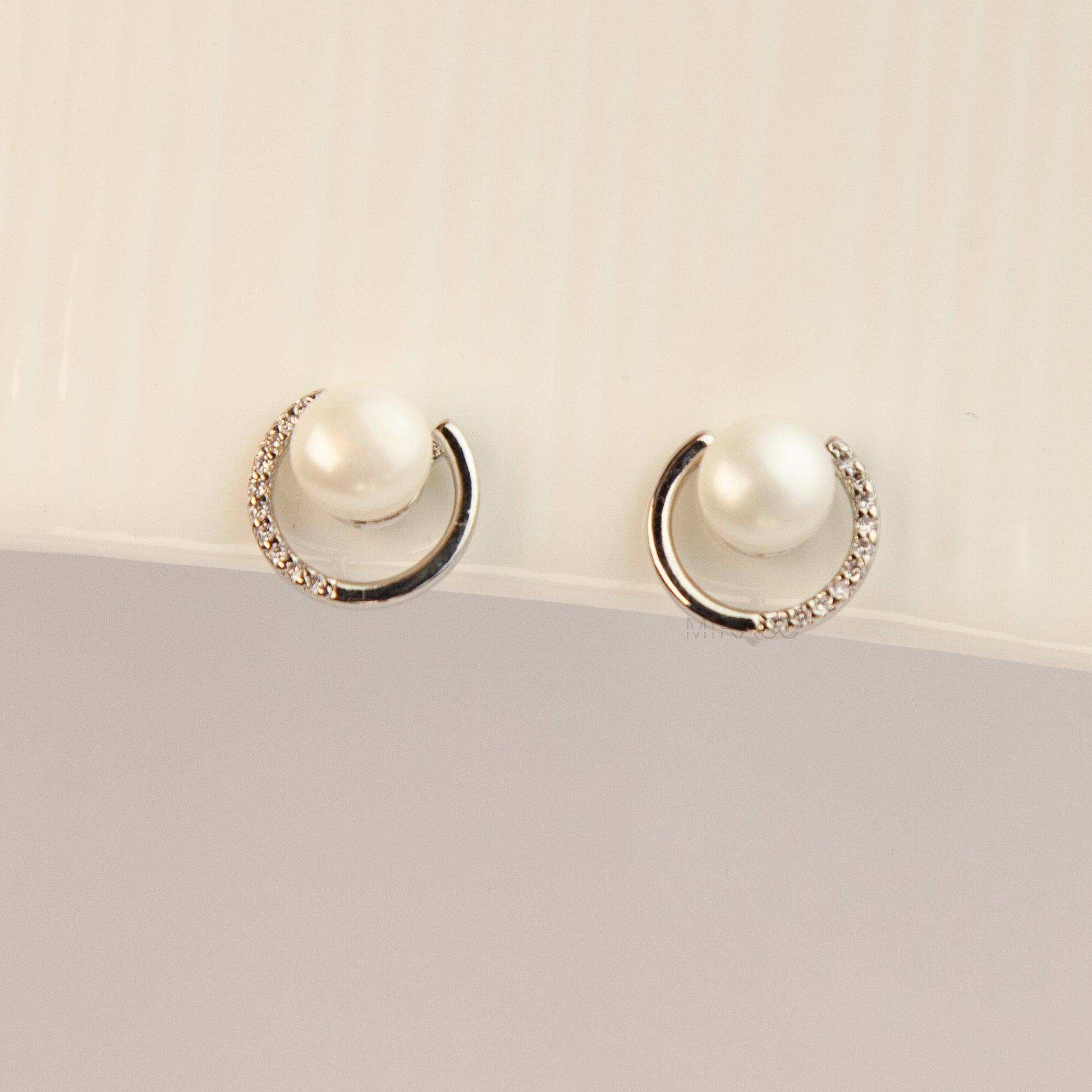 Pair of non-pierced silver-tone clip-on earrings with round silicone backs, featuring a real white freshwater pearl wrapped in a sparkling cubic zirconia crescent loop.